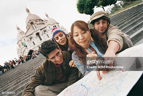 young tourist couples sitting on the steps of the sacre coeur basilica, pointing at a map, montmartre, paris, france - coeur stock pictures, royalty-free photos & images