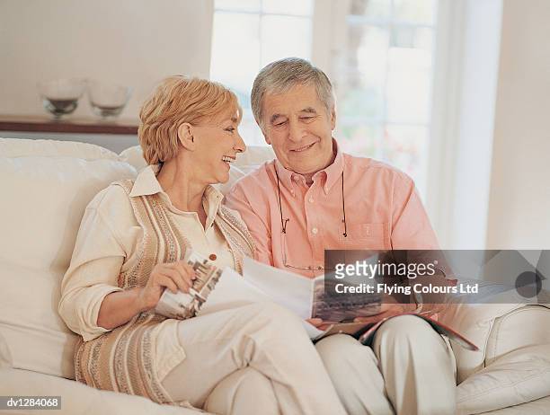 senior couple sitting at home on their sofa reading a home shopping catalogue - cephalon climbs above valeant takeover bid of 73 a share stockfoto's en -beelden
