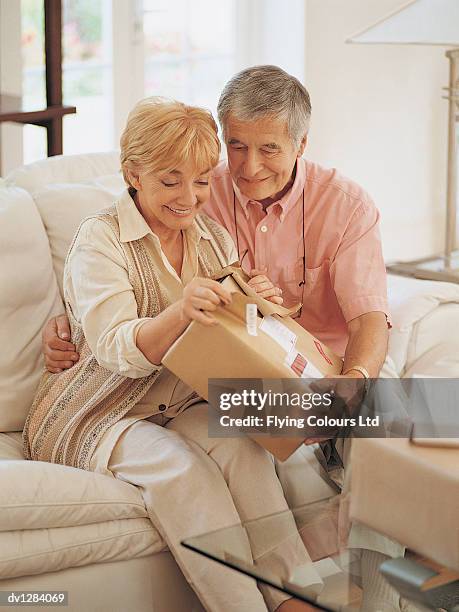senior couple sitting on a sofa at home and opening a parcel - cephalon climbs above valeant takeover bid of 73 a share stockfoto's en -beelden
