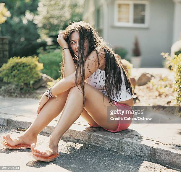 female teenager sitting on a kerb in the subururbs looking sideways - kerb fotografías e imágenes de stock