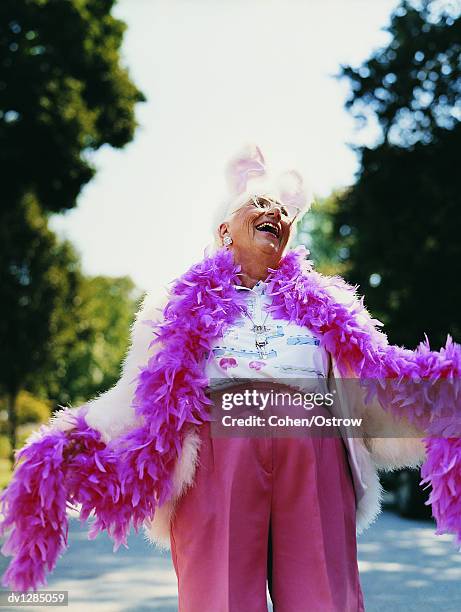 senior woman wearing a feather boa and a rabbit costume laughing and looking upwards - excéntrico fotografías e imágenes de stock