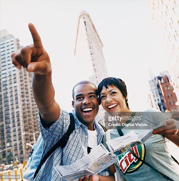 young sightseeing couple in new york pointing and standing in front of the flatiron building - national front stockfoto's en -beelden