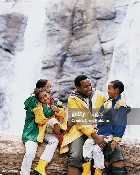 family of four sitting on a tree trunk in front of a waterfall talking - front view portrait of four children sitting on rock stock pictures, royalty-free photos & images