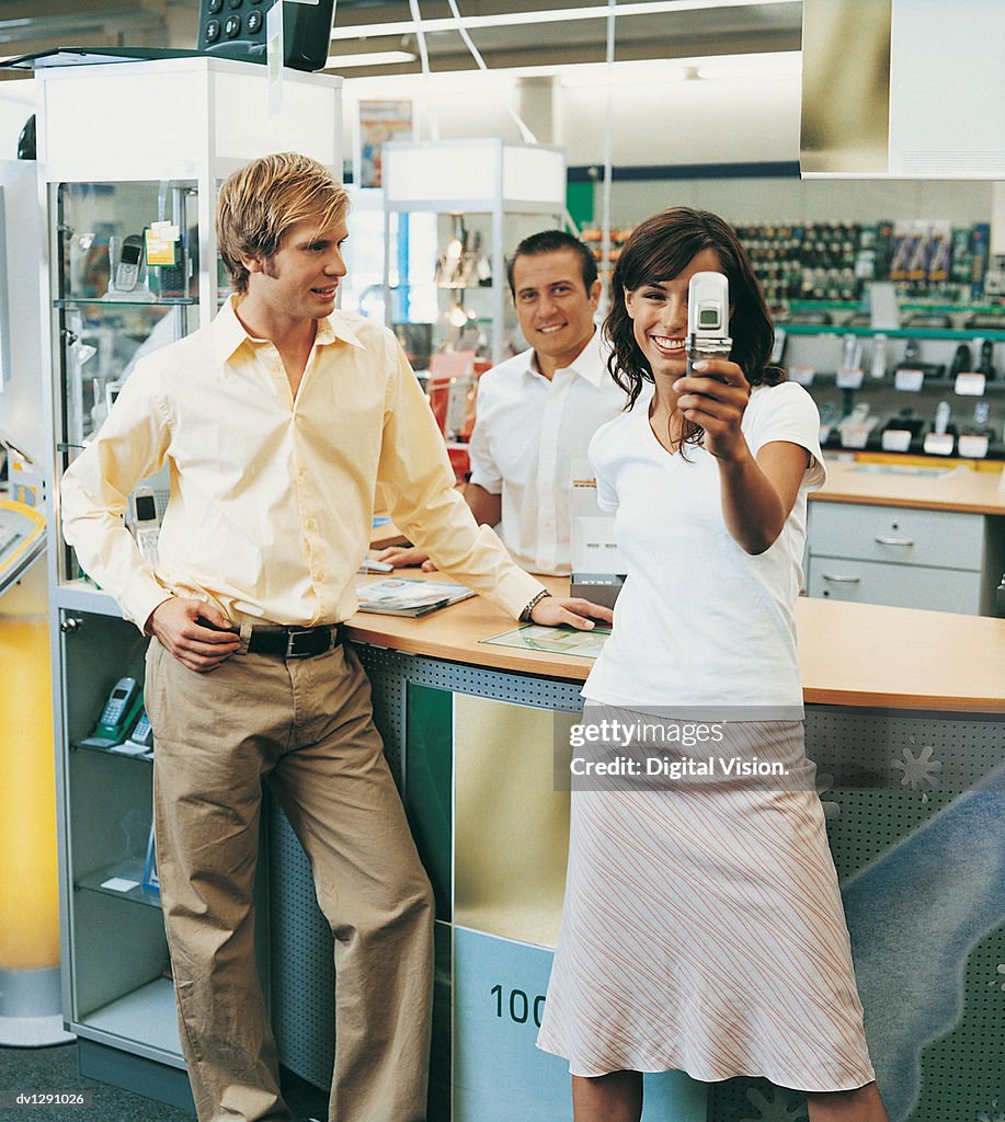 Young Woman Looking at a Video Phone in Front of the Checkout Counter of a Mobile Phone Shop