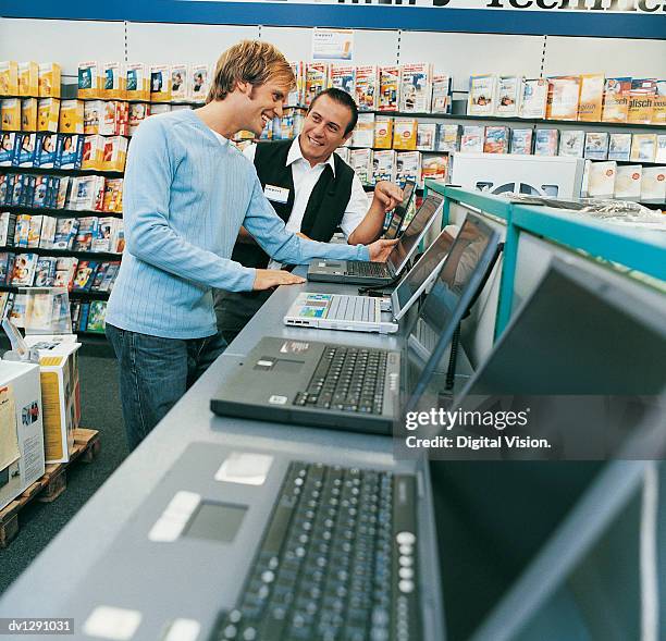 shop assistant helping a customer with a laptop in a computer shop - computer store photos et images de collection