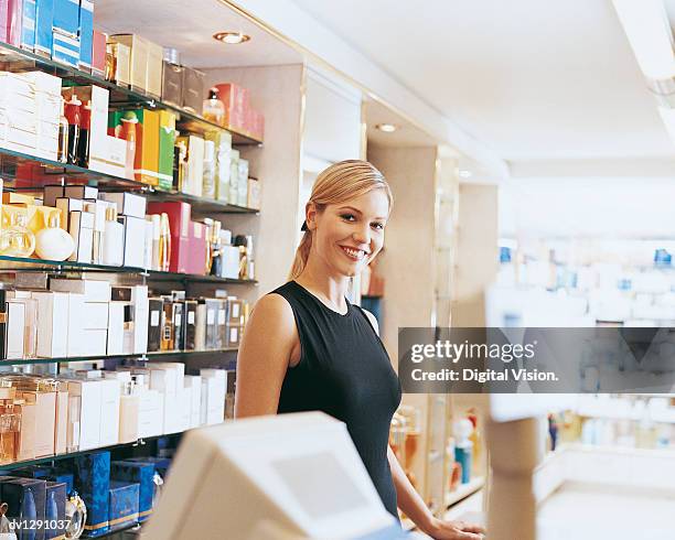 shop assistant stands behind perfume counter smiling at camera - perfumería fotografías e imágenes de stock