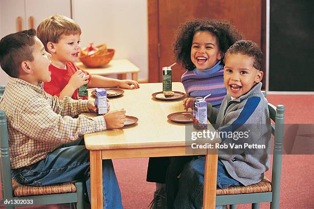 four nursery school children sitting at a table for a snack - juice box stock pictures, royalty-free photos & images