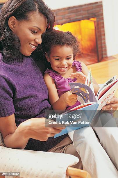 mother and daughter sitting reading a picture book together - bedtime stories stock-fotos und bilder