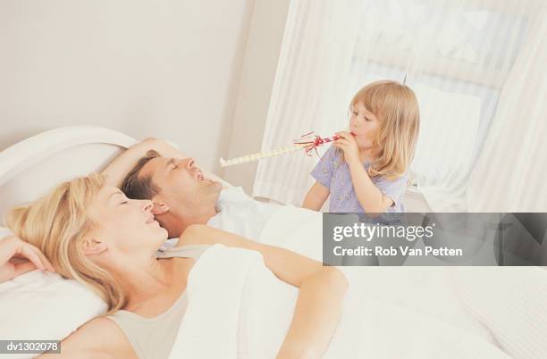 girl blowing party hooter at sleeping parents waking them up - bedside table kid asleep stock pictures, royalty-free photos & images