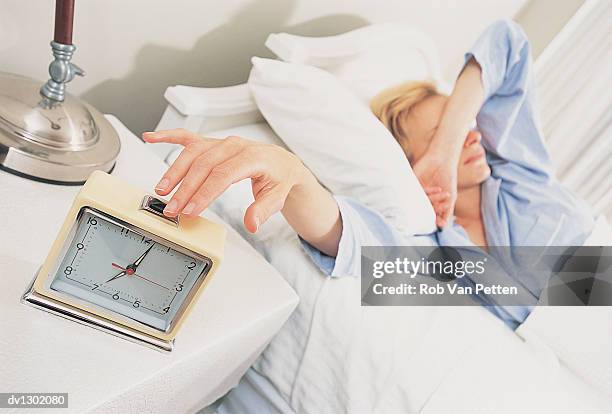 woman lying in bed with arm over face and stretching for alarm clock - rob cross stock pictures, royalty-free photos & images