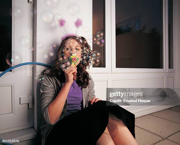 portrait of a young girl wearing a deely bopper and sitting against a wall and blowing bubbles from a bubble wand - haarreifen mit sternchen stock-fotos und bilder