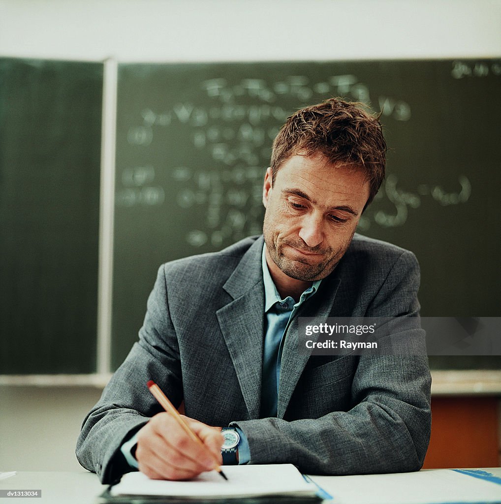 https://media.gettyimages.com/id/dv1313034/photo/tired-male-teacher-sitting-behind-a-desk-working.jpg?s=1024x1024&amp;w=gi&amp;k=20&amp;c=_PR5YKEM0VI7xecHfd_lBH7YSwYlTC49j7LUXcIoU0g=