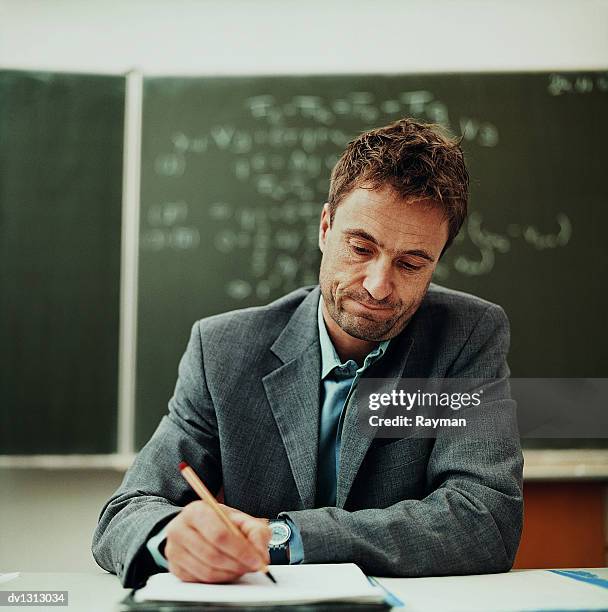 tired male teacher sitting behind a desk working - teacher desk stock pictures, royalty-free photos & images