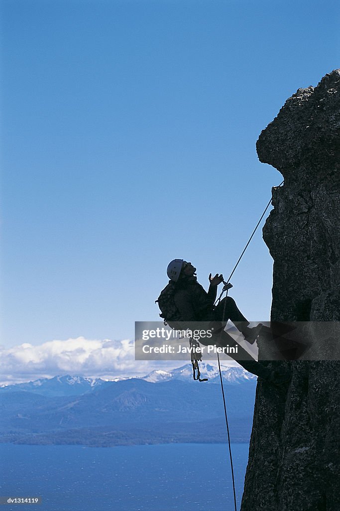 Young Man Climbing Vertical Rock Face High Above Valley