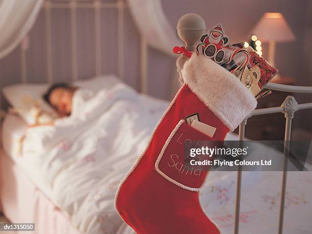 christmas stocking hanging on a bed knob and a child sleeping in bed in the background - stockings fotos stock-fotos und bilder