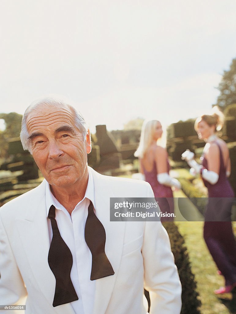 Portrait of a Senior Man Walking in a Formal Garden With Women in the Background