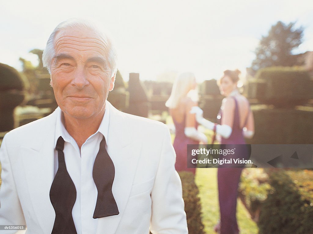 Portrait of a Senior Man in a Formal Garden With Women in the Background