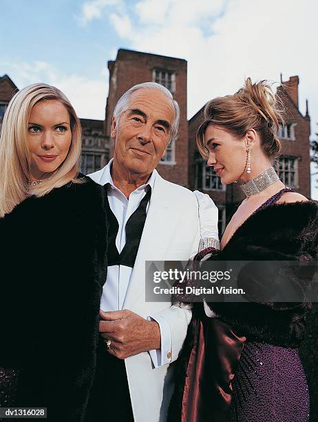 portrait of a wealthy senior man standing between two young women - manteau de fourrure photos et images de collection