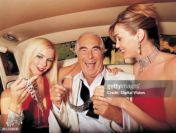 wealthy senior man sitting between young women in the back of a limousine - símbolo de status imagens e fotografias de stock