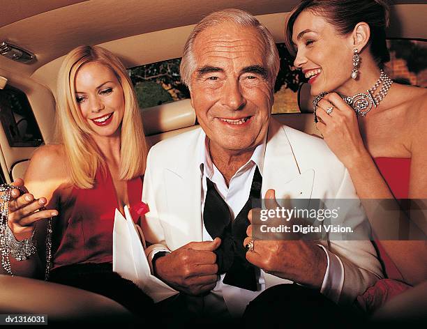 wealthy senior man sitting between young women in the back of a limousine - untied stock pictures, royalty-free photos & images