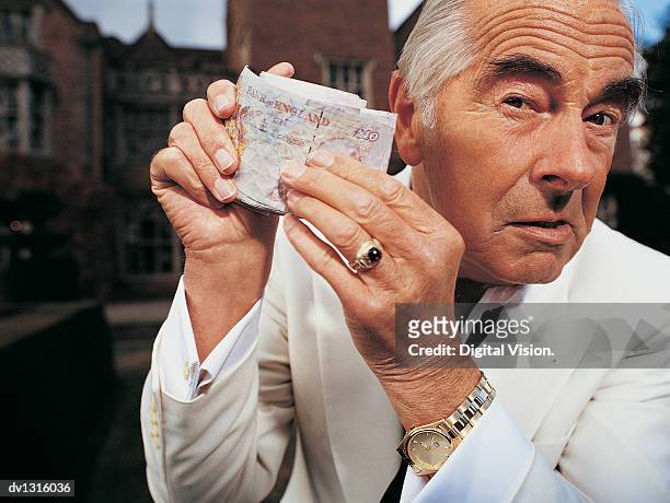 portrait of a senior man holding a wad of money - ten pound note - fotografias e filmes do acervo