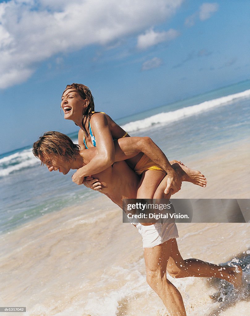 Young Man Giving a Woman a Piggback on a Beach
