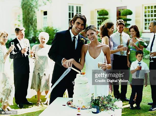 portrait of the smiling bride and groom cutting a wedding a cake at the reception - wedding cakes stock pictures, royalty-free photos & images