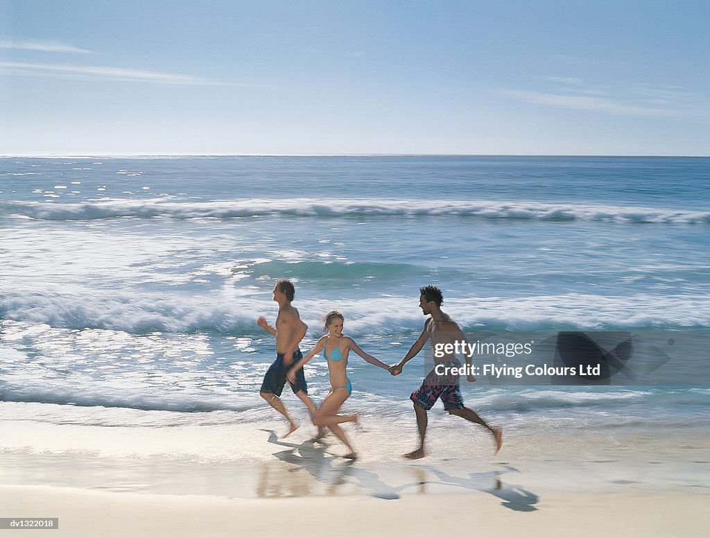 Three Young Adults Running at the Water's Edge Along An Empty Beach