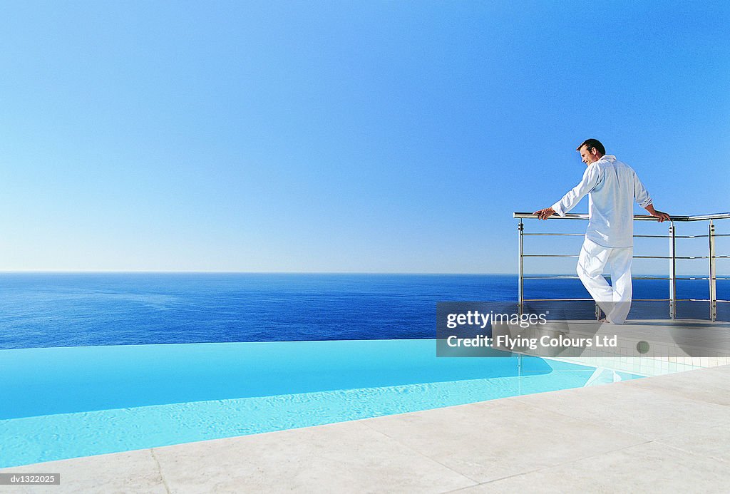 Man Standing Leaning on Railing Looking at View Over Sea