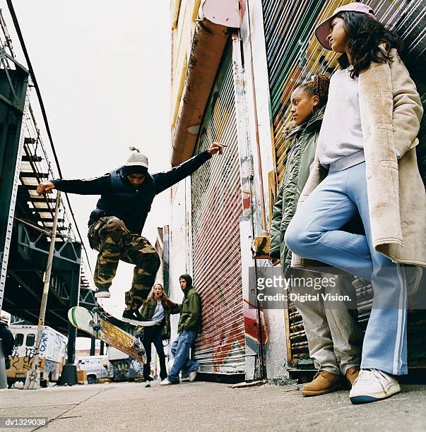 medium group of teenagers in a back alley watching stunts on a skateboard - medium group of people foto e immagini stock