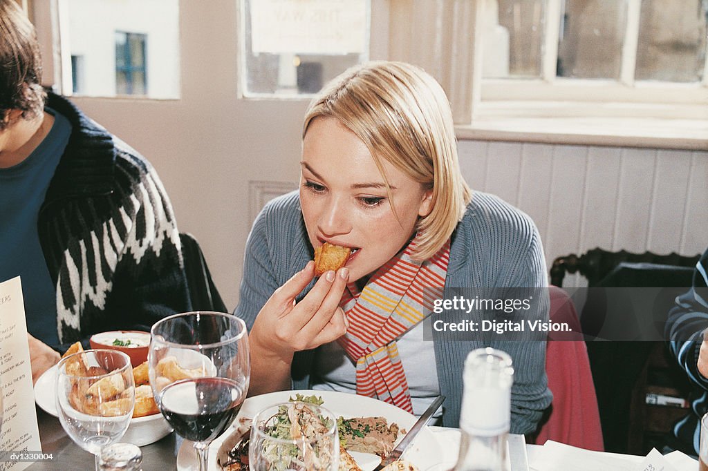 Woman Sitting in a Restaurant Eating a Roast Potato