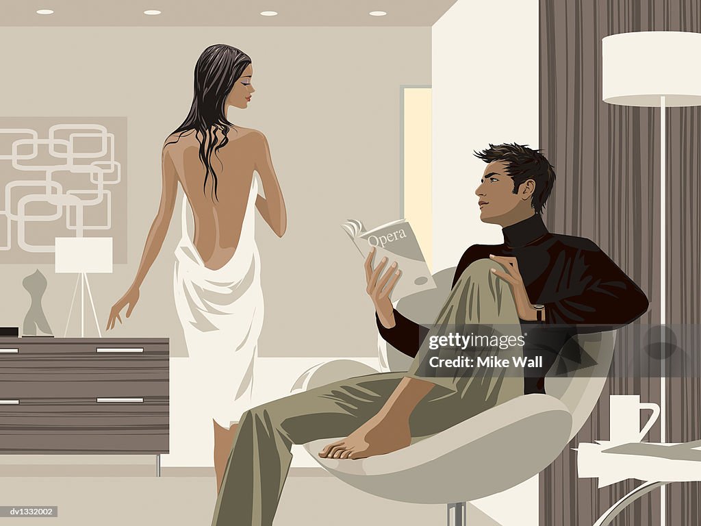 Man Sitting in an Armchair in a Living Room Contemplating and Holding a Book and a Woman Standing Wrapped in a Towel