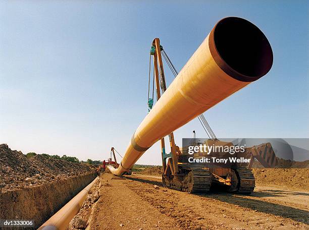 construction vehicle lowering a long pipeline into a trench in a dirt road - pipeline road stock pictures, royalty-free photos & images