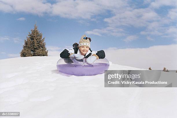 young boy sledding down a snow-covered hill on a rubber ring - rubber ring stock-fotos und bilder