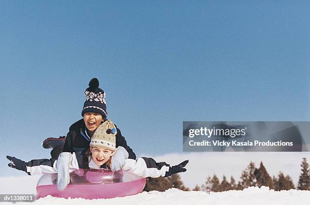 two children sledding on a rubber ring in the snow - rubber ring stock-fotos und bilder