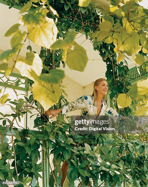 smiling, young woman standing on a ivy covered balcony looking at the view - creeper stock-fotos und bilder