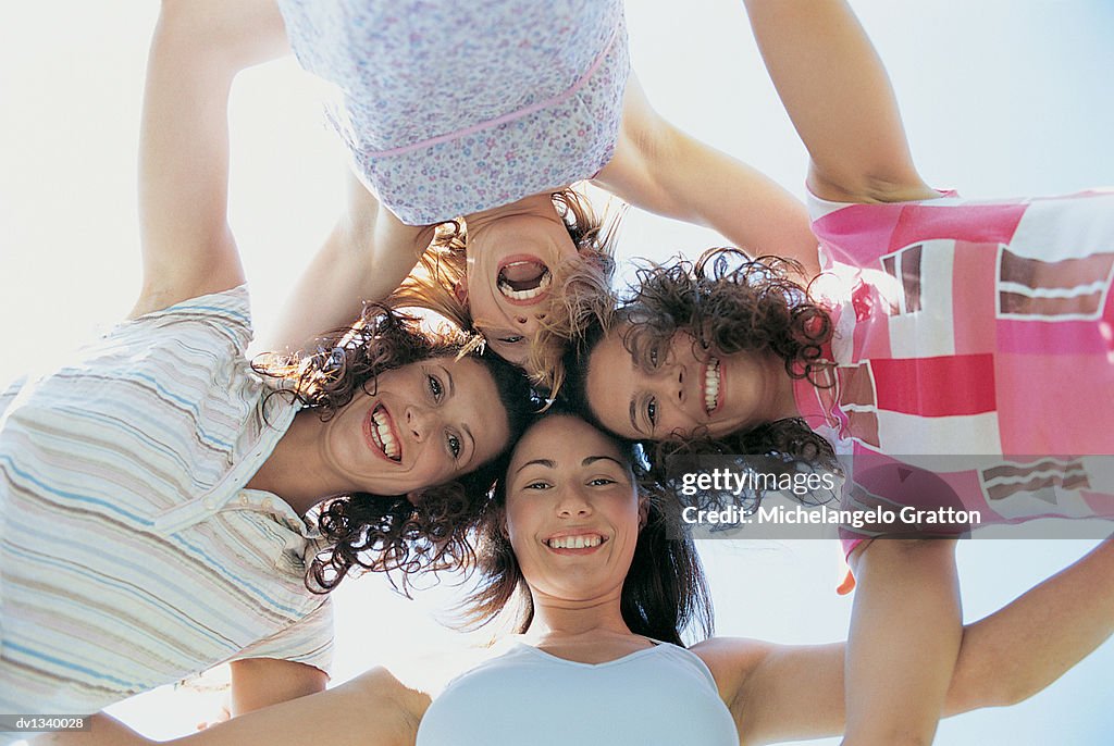 Portrait of Four Smiling, Young Women Looking Down With their Arms Around Each Other