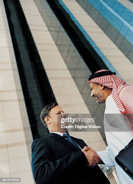 two businessmen shaking hands by a glass wall in the city - low angle view of two businessmen standing face to face outdoors stock pictures, royalty-free photos & images