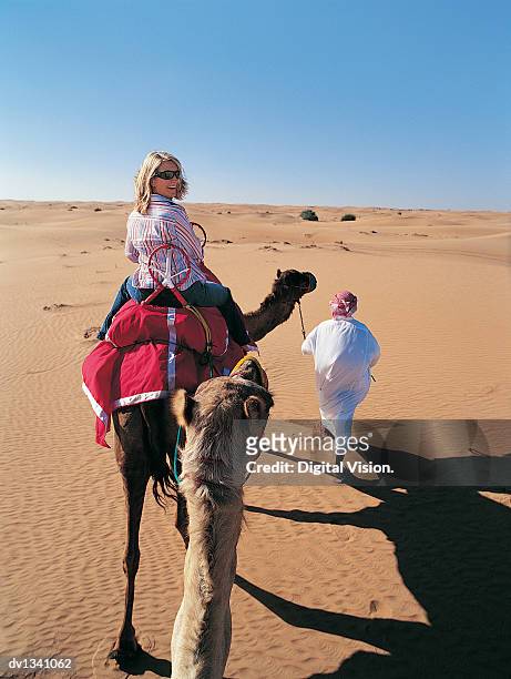 woman riding a camel following a man in traditional middle eastern dress - eastern european descent stockfoto's en -beelden