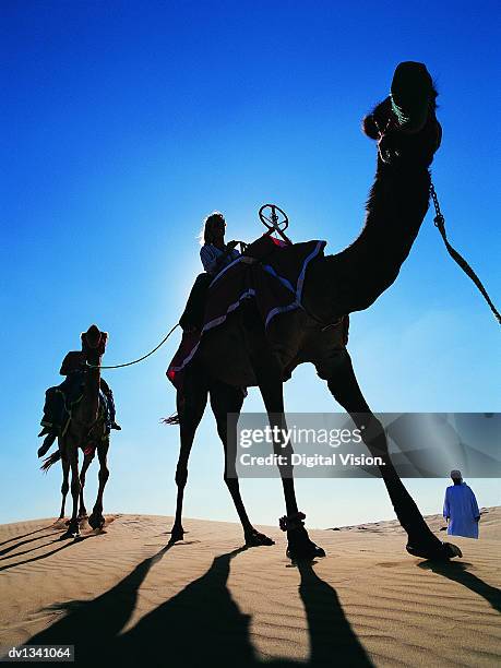 couple travelling across the desert on camel with a man wearing traditional middle eastern dress - eastern european descent stockfoto's en -beelden