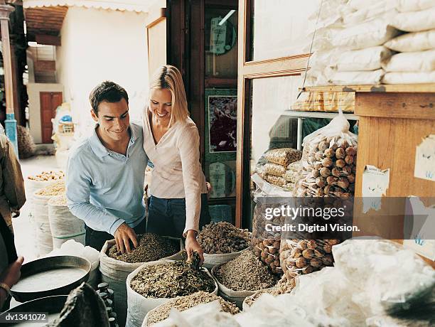 couple on holiday looking down at sacks full of spices in a market stall at a souk, dubai - souk foto e immagini stock