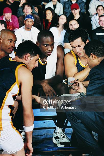 sports coach giving his basketball players a pep talk in a basketball court in front of the audience in the stands - team talk stockfoto's en -beelden