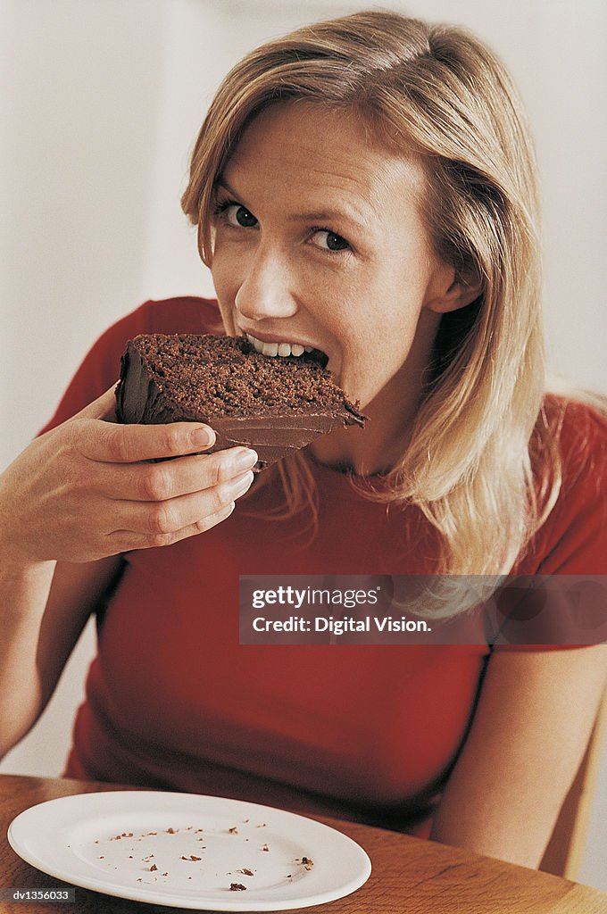 Woman Sitting at Table and Biting Into a Slice of Chocolate Cake