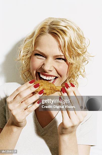 portrait of a smiling, young woman eating a deep fried chicken drumstick - deep fried fotografías e imágenes de stock