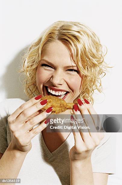 portrait of a smiling, young woman eating a deep fried chicken drumstick - woman eating chicken photos et images de collection