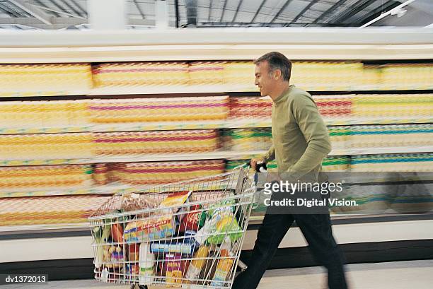 man pushing a shopping trolley quickly down a supermarket aisle - men bulge imagens e fotografias de stock