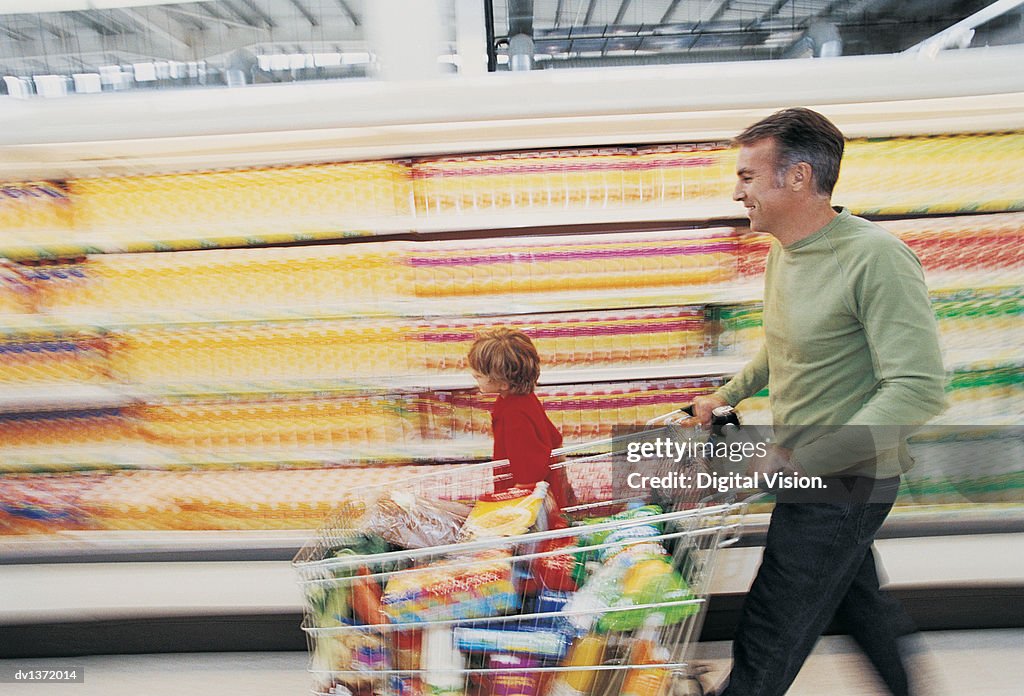 Man Pushing a Shopping Trolley Quickly Down a Supermarket Aisle With His Son