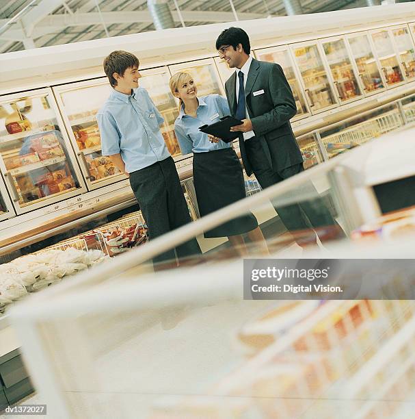 manager organising his shop assistants in the frozen food aisle of a supermarket - boss nameplate stock pictures, royalty-free photos & images