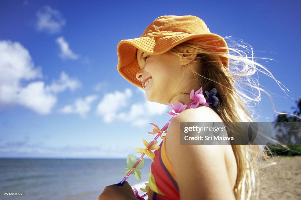 Young Girl Wearing A Sunhat And A Garland Stands On The Beach