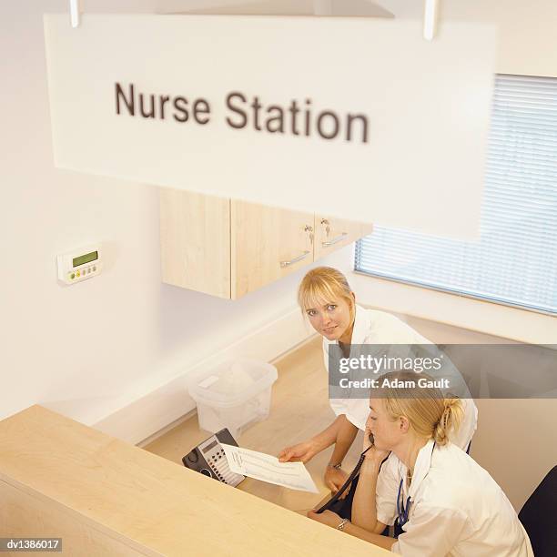 two nurses working at a reception desk behind an information sign in a hospital - escrita ocidental imagens e fotografias de stock